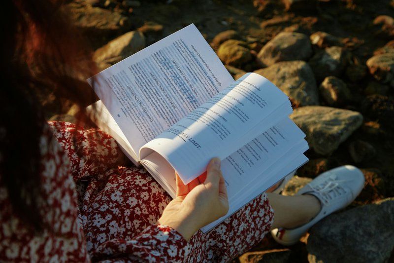 A woman reading a book while sitting on rocks